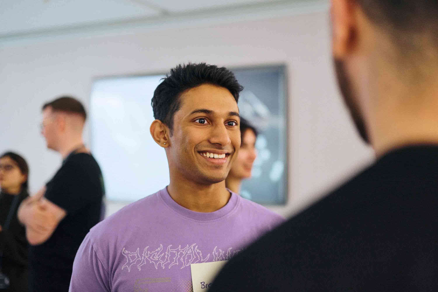 Male with dark hair and in a purple t-shirt smiling to someone off camera