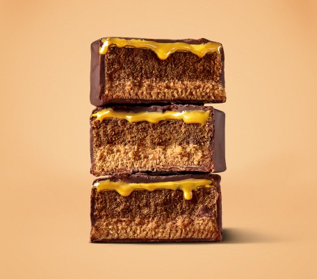 Three halves of Myprotein carb crusher bars, stacked on top of one another so that we can see the gooey caramel and nougat 