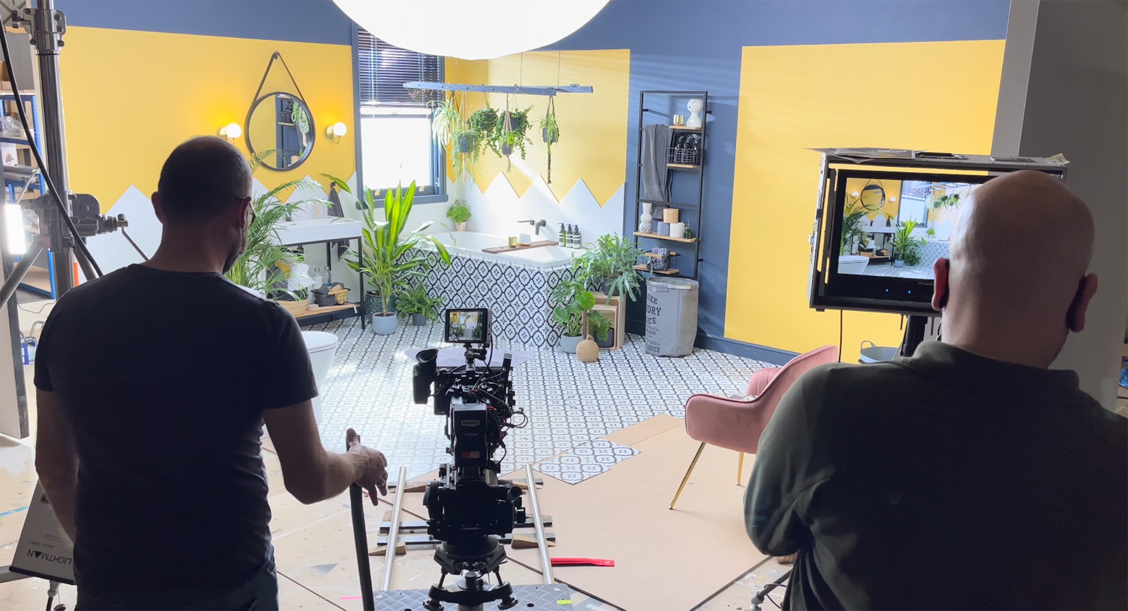 Behind the scenes view of two cameramen on a yellow bathroom interior studio shoot.