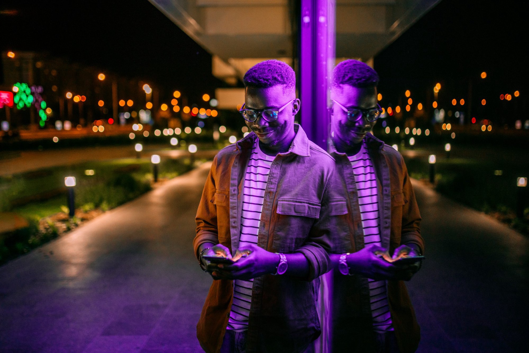 A man looking at his phone standing under a purple light